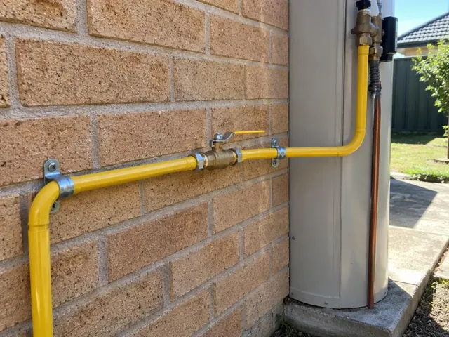 Yellow gas pipe and valve on a brick wall beside a hot water unit in Canley Heights