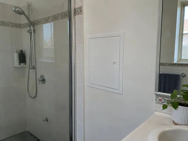 Bathroom wall with a small access panel beside a shower and tiled surround in Cabramatta